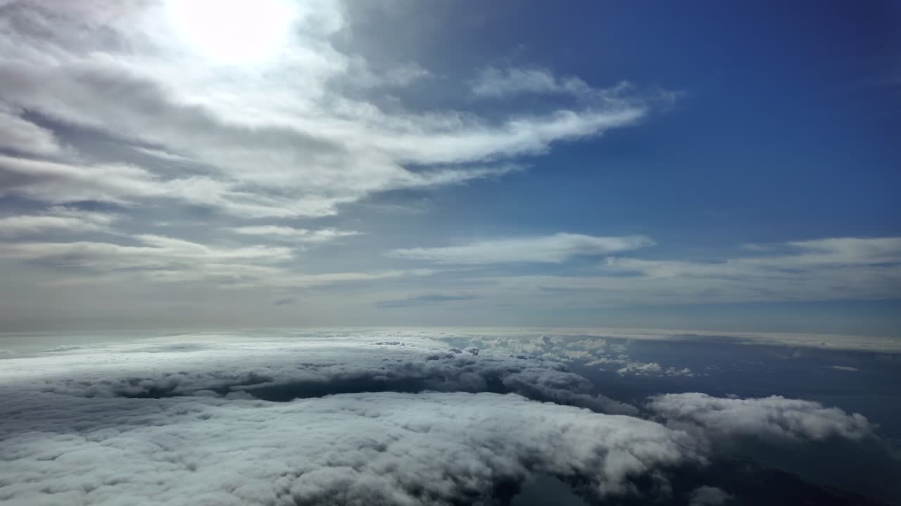 A dreamy clopudscape captured from a jet cockpit while flying through peaceful skies between layers of ethereal stratus clouds and a radiant and veiled sun shining above in a blue sky