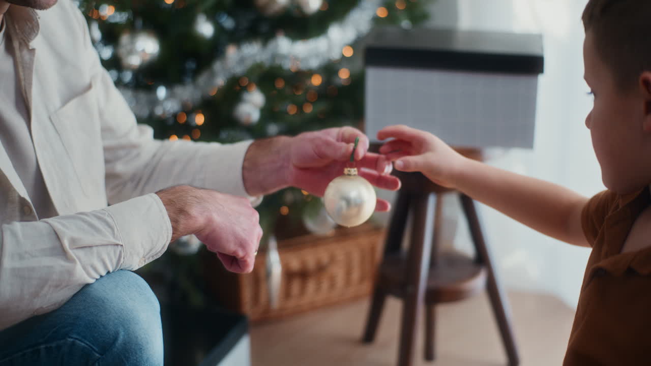 el niño le da a su padre una joya de navidad de vidrio y decoran el árbol de navidad.