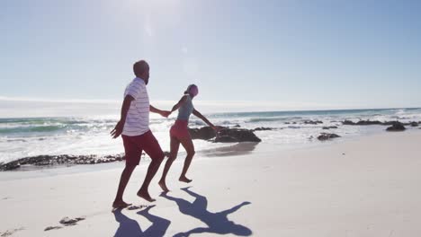 african american couple holding hands and running on the beach
