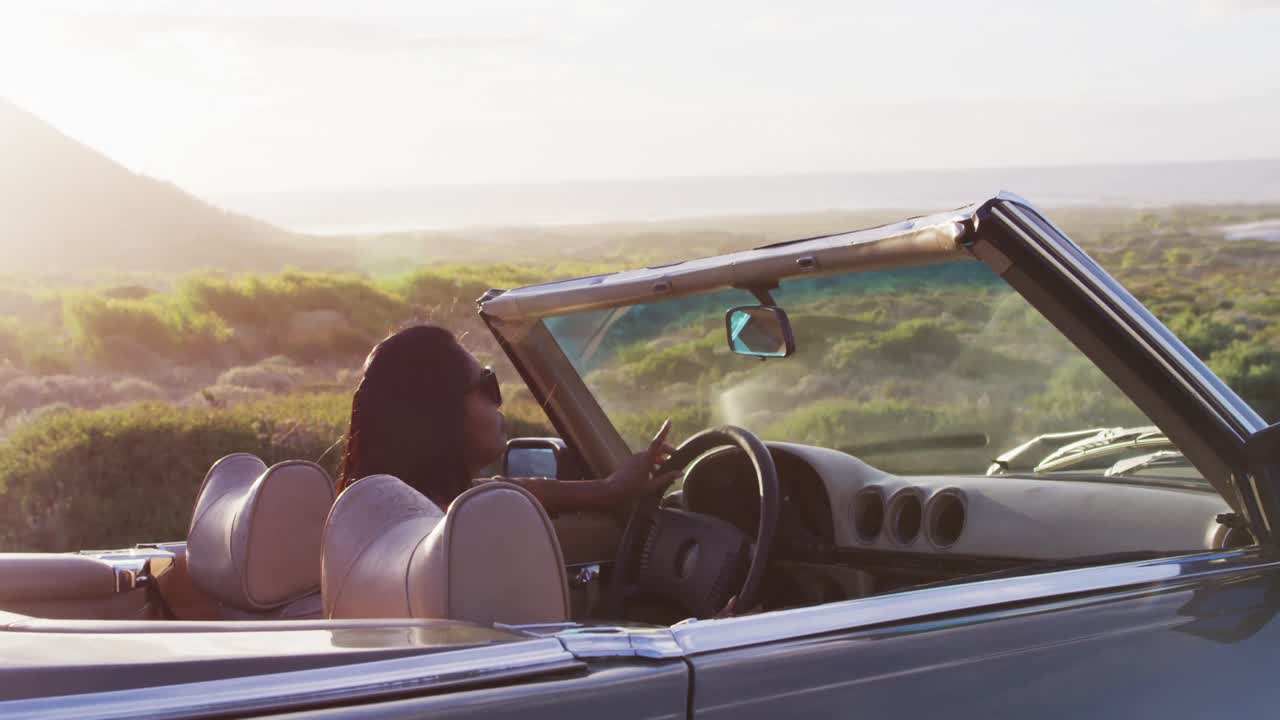mujer afroamericana conduciendo por una carretera de campo en un coche descapotable