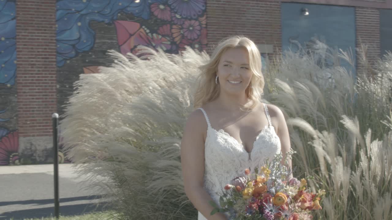 novia sonriente sosteniendo un ramo de flores con plantas de largo ondulado como fondo