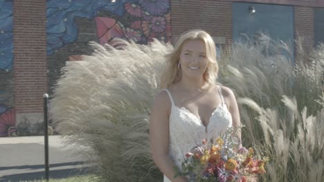novia sonriente sosteniendo un ramo de flores con plantas de largo ondulado como fondo
