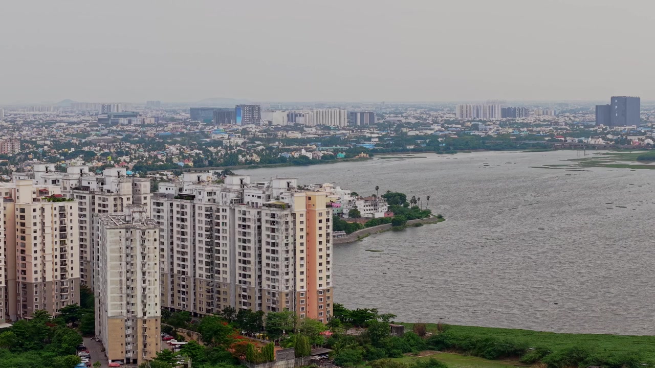 Ripresa aerea con drone che mostra grattacieli residenziali accanto a un grande specchio d'acqua con vegetazione e un denso paesaggio urbano residenziale a Chennai, Tamil Nadu, India, durante il giorno.