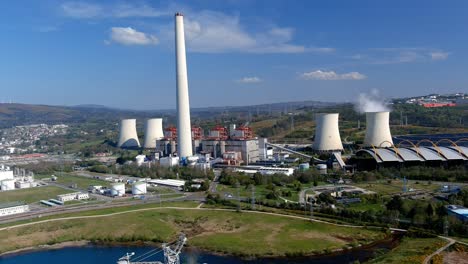 Thermal-power-plant-with-smoking-chimney,-lake-in-front-with-an-old-excavation-machine,-the-village-next-door,-bright-and-sunny-afternoon