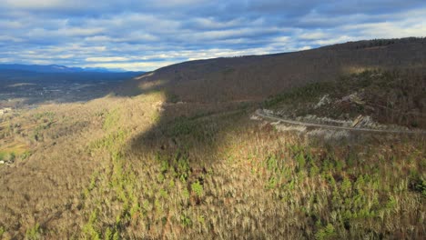 Eine-Drohne,-Die-Seitwärts-über-Ein-Bergtal-Fliegt,-Wobei-Wolken-Im-Spätherbst-Schatten-Auf-Die-Hügel-Und-Das-Darunter-Liegende-Tal-Werfen