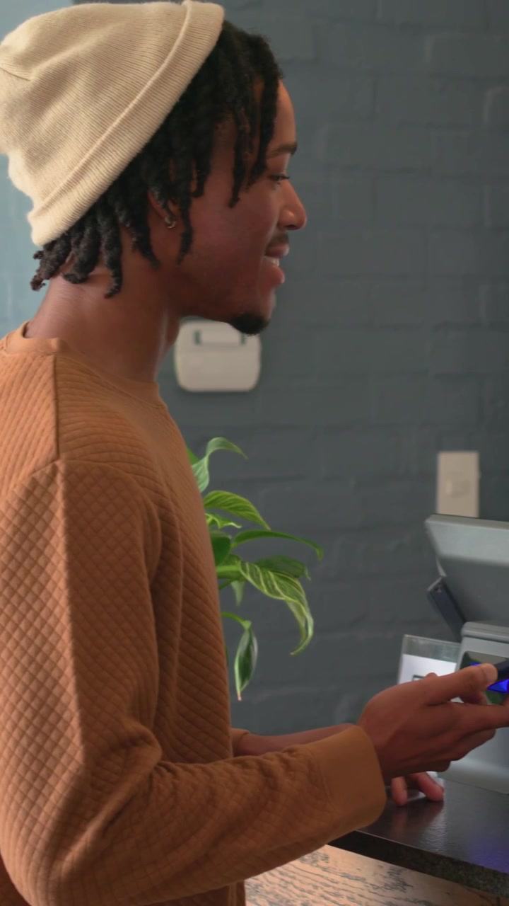 Vertical video: Talking to staff, man in beanie and sweater leaning at cafe tapping reader paying