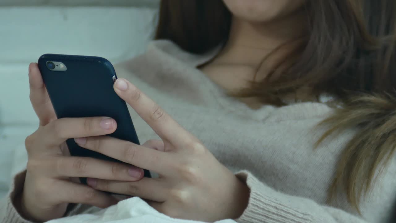 Happy Asian women are using smart phone on the bed in morning. Asian woman in bed checking social apps with smartphone. Smiling woman surfing net with cellphone at home. Mobile addict concept.