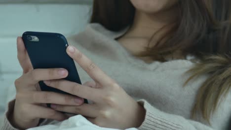 las mujeres asiáticas felices están usando el teléfono inteligente en la cama por la mañana. la mujer asiática en la cama revisando aplicaciones sociales con el teléfono inteligente. la mujer sonriente navegando por la red con el teléfono celular en casa.