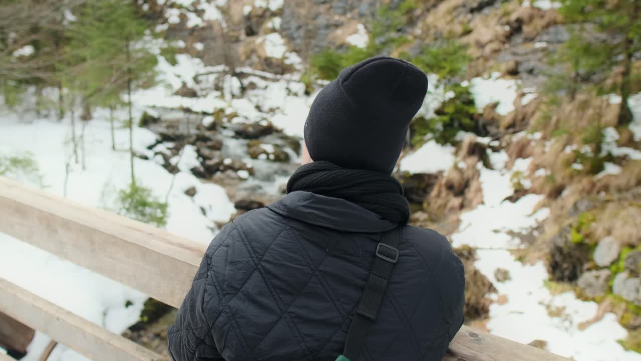 Person standing on a wooden bridge in a snowy mountain landscape