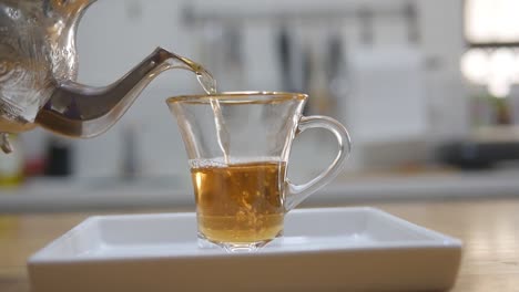 Person-is-pouring-a-cup-of-tea-until-it-over-floats,-outdoor-footage-with-blurred-building-in-the-background,-daytime-capture