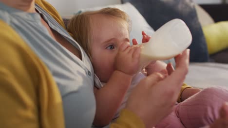 mid section of caucasian mother feeding milk to her baby in the bed at home