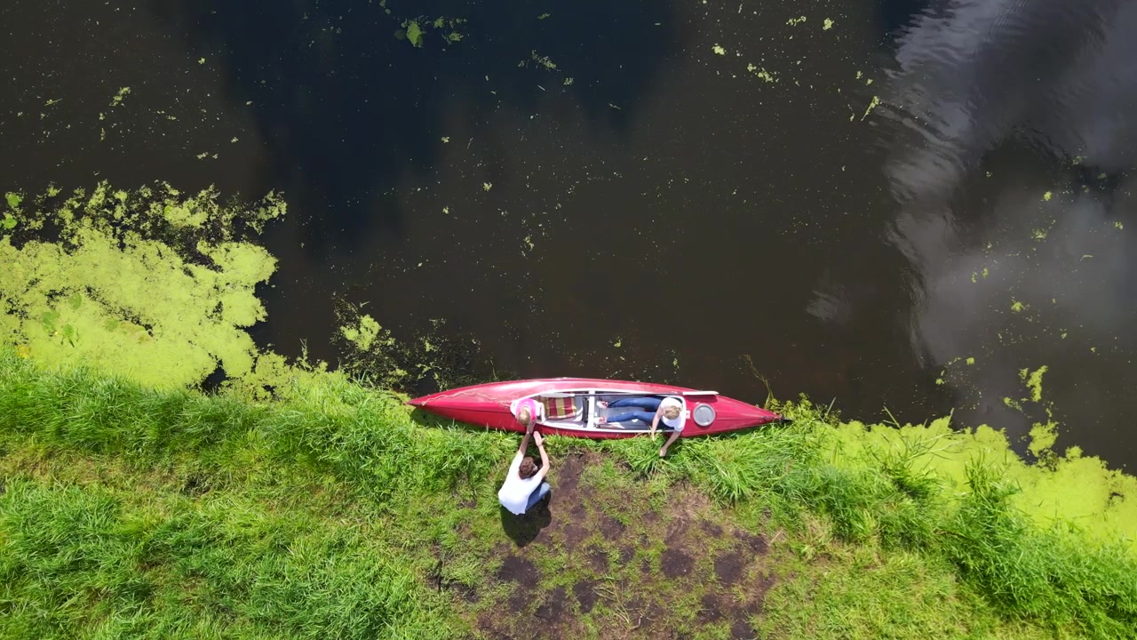 Miglior volo aereo dall'alto. Vacanza in famiglia: madre con bambino su barca a pedali rossa su fiume naturale, estate 2023 Germania. Ripresa verticale con drone a volo d'uccello 4K cinematografico