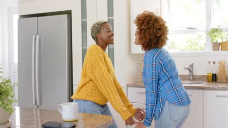 Happy-diverse-female-lesbian-couple-dancing-in-kitchen-in-slow-motion