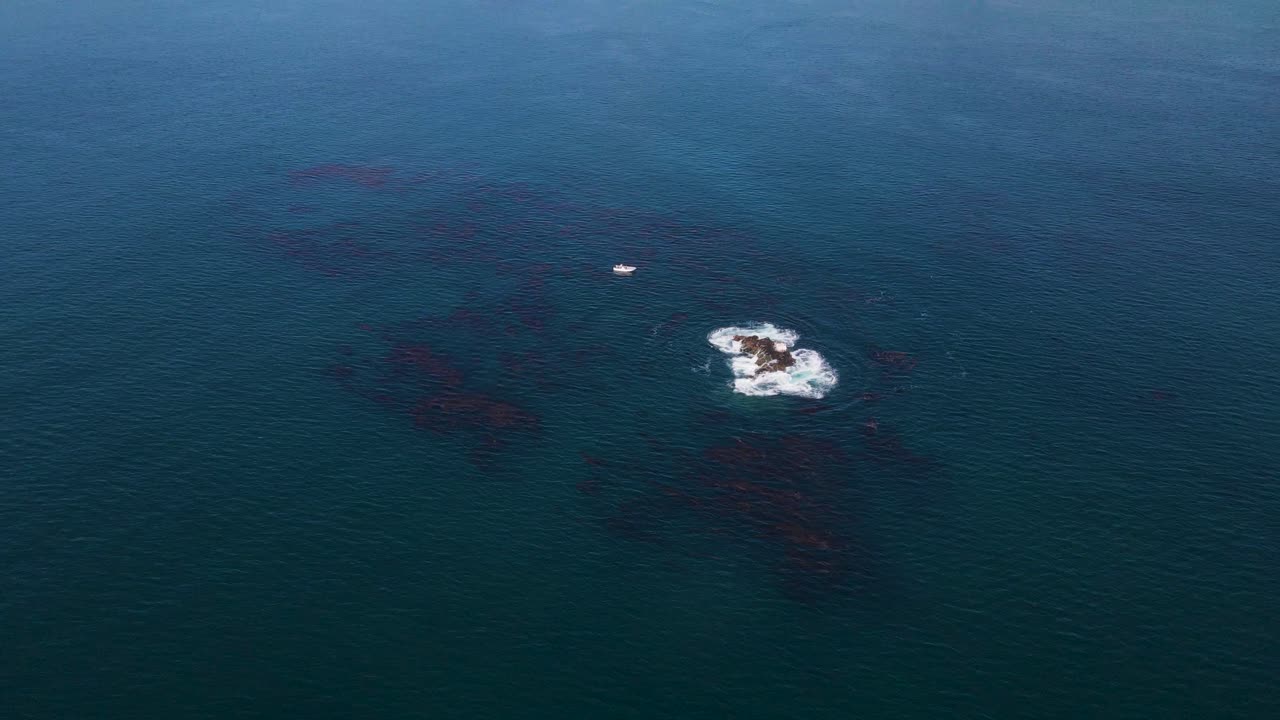A boat anchored at Cedros Island with tranquil ocean waves under soft midday light next to shallow rocks hiding below surface