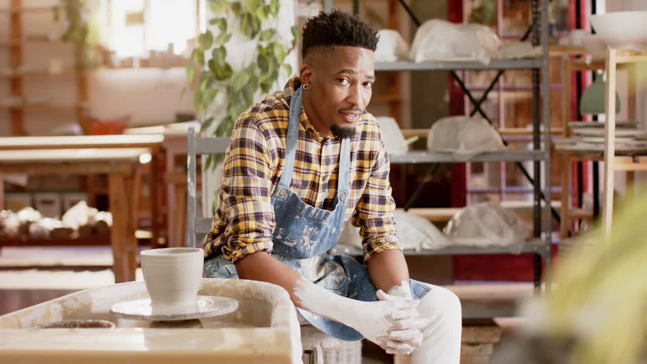 Happy african american male potter resting and smiling in pottery studio, slow motion
