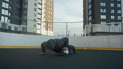 sportsman performing dynamic push-ups alternating hand placement on soccer ball, showcasing strength, coordination, and agility, background includes goal post and residential buildings