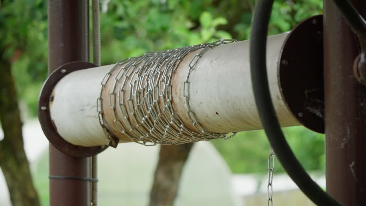 Industrial detail of heavy chain wrapped around white pipe winch for manual water well. Traditional rustic technology used in rural areas of Latvia for fetching groundwater on farm