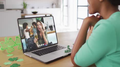 Smiling-caucasian-woman-with-beer-wearing-clover-shape-band-on-video-call-on-laptop