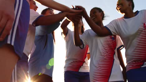 Female-soccer-team-clasping-hands-together-on-soccer-field.-4k