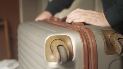 person zips grey suitcase shut and carries out of frame, close up