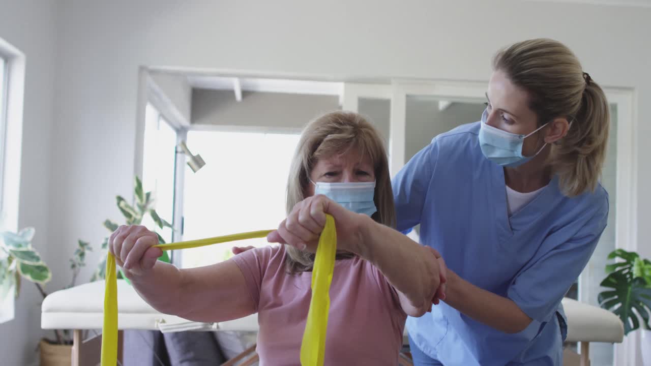 Female health worker assisting senior woman to exercise with exercise band at home