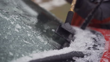 man cleaning and scraping ice from car windshield in snow slowmo