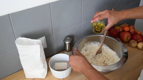 Mediterranean-Man-Hand-pour-a-glass-of-extra-vergine-olive-over-white-flour-inside-metal-bowl