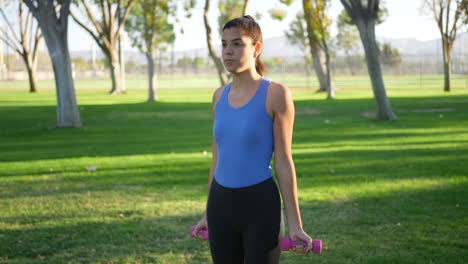 Eine-Junge-Frau,-Die-Im-Park-Ein-Hanteltraining-Macht-Und-Bizeps-Curls-Durchführt,-Um-Armmuskeln-Aufzubauen-Und-Zeitlupe-Zu-Stärken