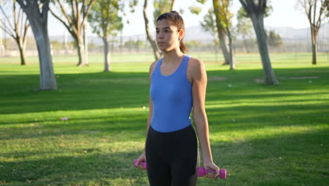 una mujer joven haciendo un entrenamiento con mancuernas en el parque realizando rizos de bíceps para construir músculo del brazo y fuerza a cámara lenta