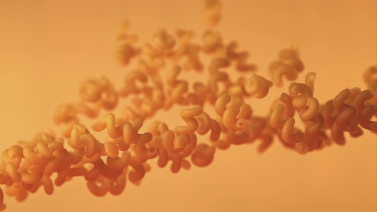 Pasta fusilli cruda che galleggia e cade su uno sfondo arancione caldo