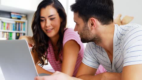 pareja interactuando entre sí mientras usan una computadora portátil en la cama