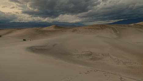 slow pan downward from the cloudy sky to wet sand dunes, with footprints in the sand