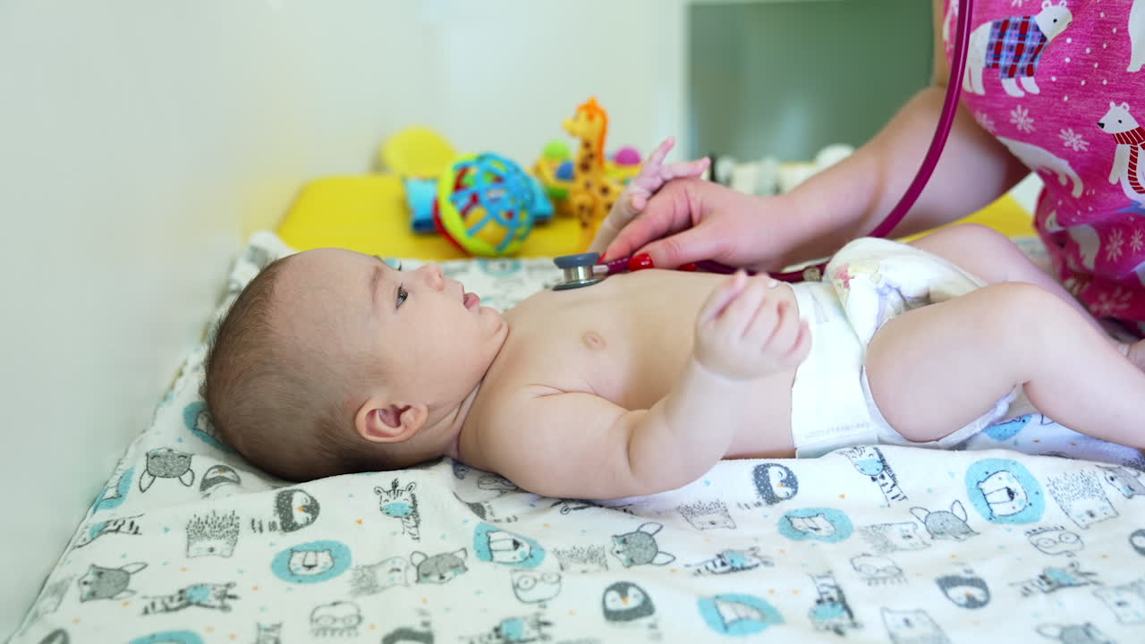 Caucasian healthy toddler in a diaper is at doctor's table. Pediatrician checking the baby with stethoscope. Close up.