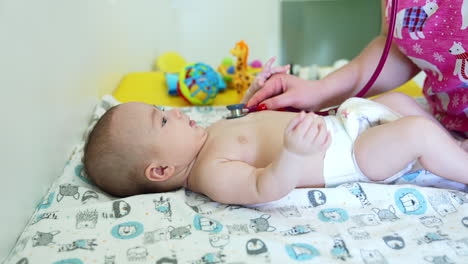 caucasian healthy toddler in a diaper is at doctor's table. pediatrician checking the baby with stethoscope. close up.