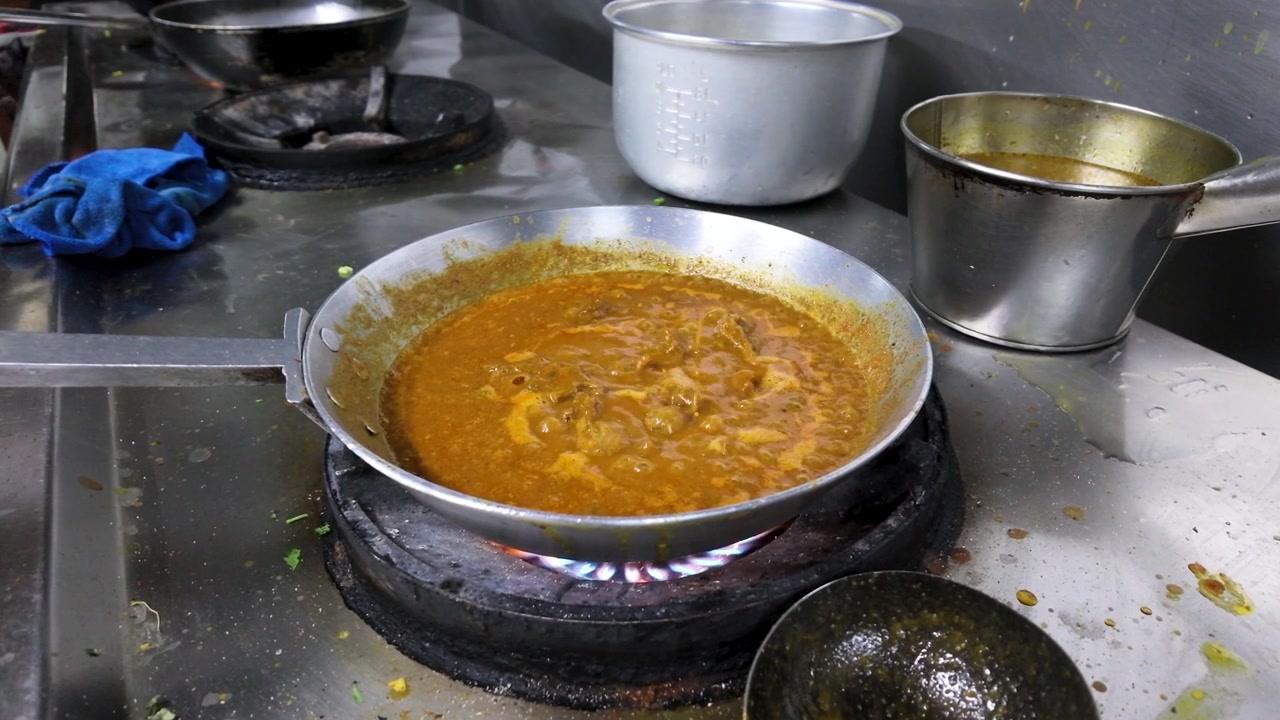 Primo piano di curry arancione che sobbolle in una padella su un fornello a gas a Bangkok.