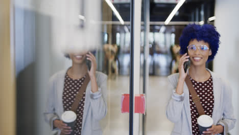 biracial businesswoman with blue afro talking on smartphone in office, slow motion