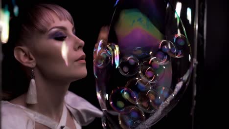close-up pretty girl does tricks with soap bubbles she blows a lot of small bubbles into one big bubble