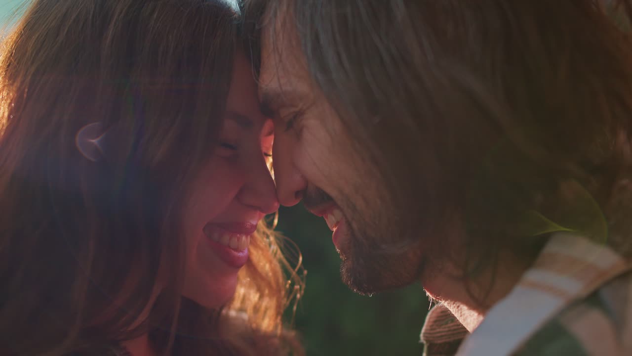 Close-up shot of a happy couple, a guy and a brunette girl rub their noses against each other and communicate during their picnic outside the city in the summer near the trailer