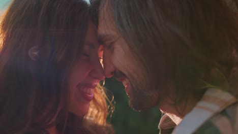 close-up de una pareja feliz, un chico y una chica morena se frotan las narices el uno contra el otro y se comunican durante su picnic fuera de la ciudad en el verano cerca del remolque