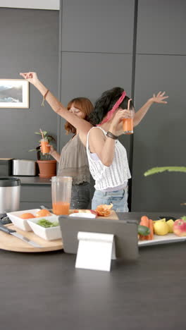 vertical video: dancing in kitchen, two women holding juice glasses and enjoying together