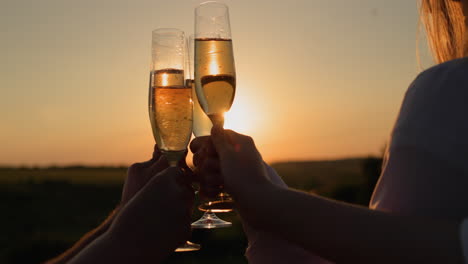 hands with glasses of champagne clink against the backdrop of a picturesque landscape where the sun sets