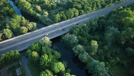 aerial top down, cars driving on rural highway bridge over river stream, surrounded by lush green trees in brunswick, germany