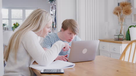 downs syndrome man sitting with female home tutor using laptop for lesson at home