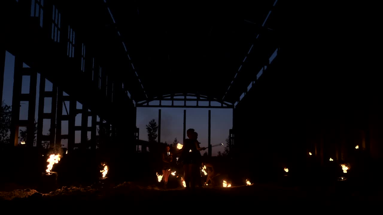 A group of people with fire and torches dancing at sunset in the hangar in slow motion. Fire show