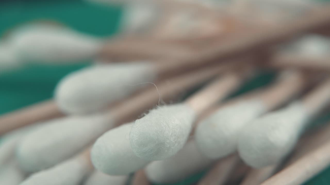 A smooth detailed macro tilt up shot of a pile of Q tips, white soft cotton tips, brown wooden sticks, professional studio lighting, teal background, 4k video