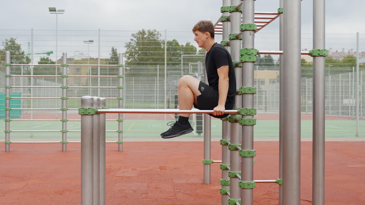Young european man doing parallel bar dips, training his upper body and core strength, focusing on fitness and a healthy lifestyle at an outdoor calisthenics park, static camera, slow motion