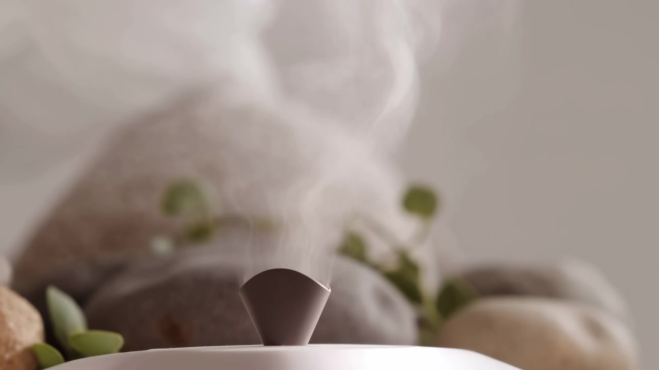 Gros plan sur la buse d'un diffuseur de table moderne libérant une fine vapeur continue vers le haut, dans une pièce douce et neutre au style spa, avec une lumière chaude et diffuse et un décor minimaliste et apaisant, incluant un diffuseur, un humidificateur et de la vapeur.