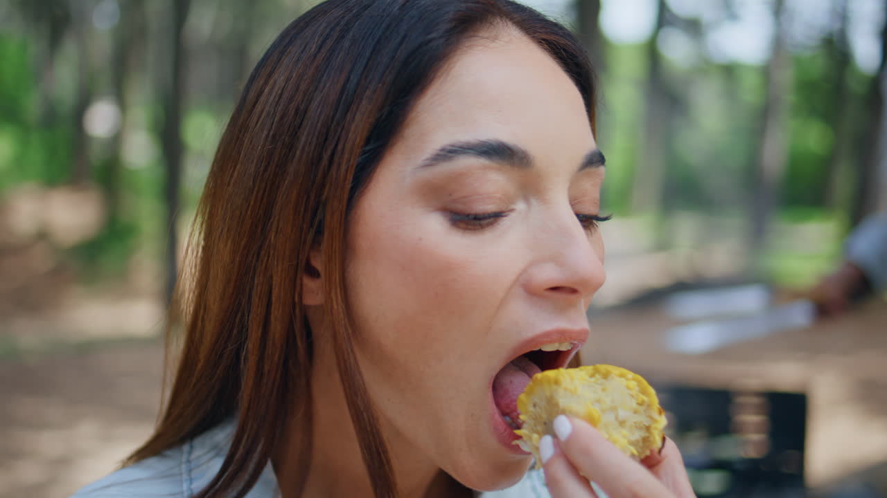 Closeup woman eating corn at summer picnic. Portrait of relaxed brunette chewing