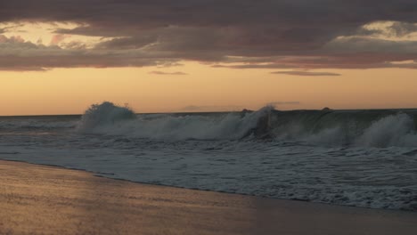 grandes olas en una playa de nueva zelanda con un amanecer dorado en el cielo.