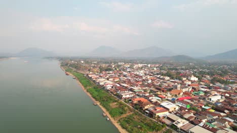 scenic aerial shot of the chiang khan district on the mekong riverside in thailand, a drone flying backward on a foggy morning